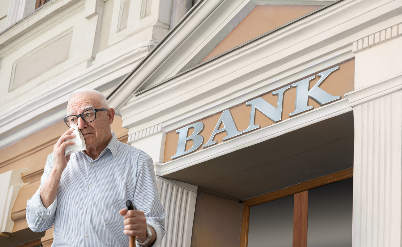 A picture of a big bank in teh background. In teh front is an older man wiping his eys. He looks very sad and worried.