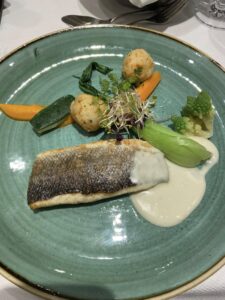 A green plate with grilled fish topped with a white sauce, potatoes and a vegetable medley.