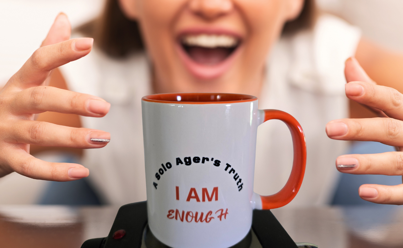 BLOG 17_Life as a Solo Plus None Can be Enough_image A woman in the background laughing as she reaches with two hands for a white coffee mug with an orange handle in the foreground wiht the saying A Solo Ager's truth I am enough inscribed on it.