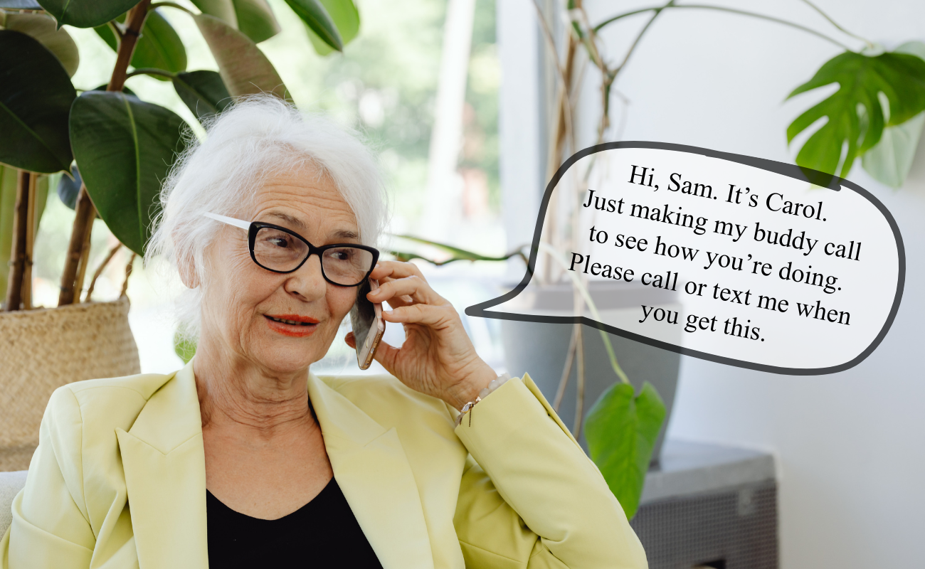 Older woman with white hair and glasses sits indoors near green houseplants, smiling while talking on a smartphone. A speech bubble reads, “Hi, Sam. It’s Carol. Just making my buddy call to see how you’re doing. Please call or text me when you get this.”