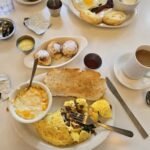 A table of breakfast foods including an omelet, a little bowl of grits, coffee, and three small round donuts.