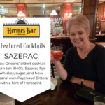 A women smiling with a cocktail in hand and a drink menu showing the bar name of Hermes Bar.