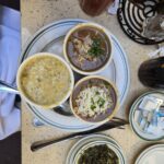 A plate fo there different cups of gumbo soup and a little dish of cooked collard greens.