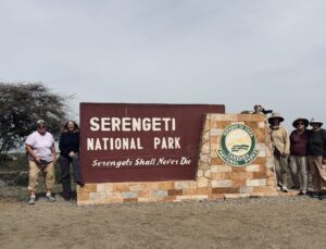 A group of women travelers on an African safari in front of the Serengeti National Park sign.