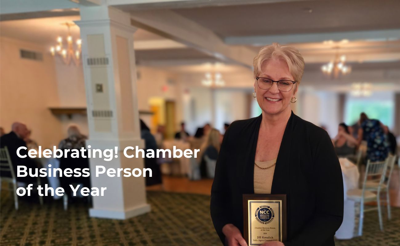 Blonde woman wearing glasses smiling holding an award plaque. Caption reads "Celebrating! Chamber Business Person of the Year."
